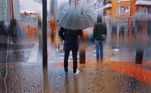 Image of a person walking under an umbrella in the rain.
