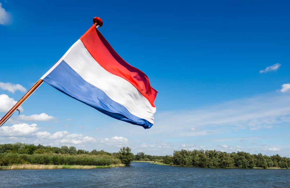 Dutch flag blowing in the wind over a large lake and grassy land