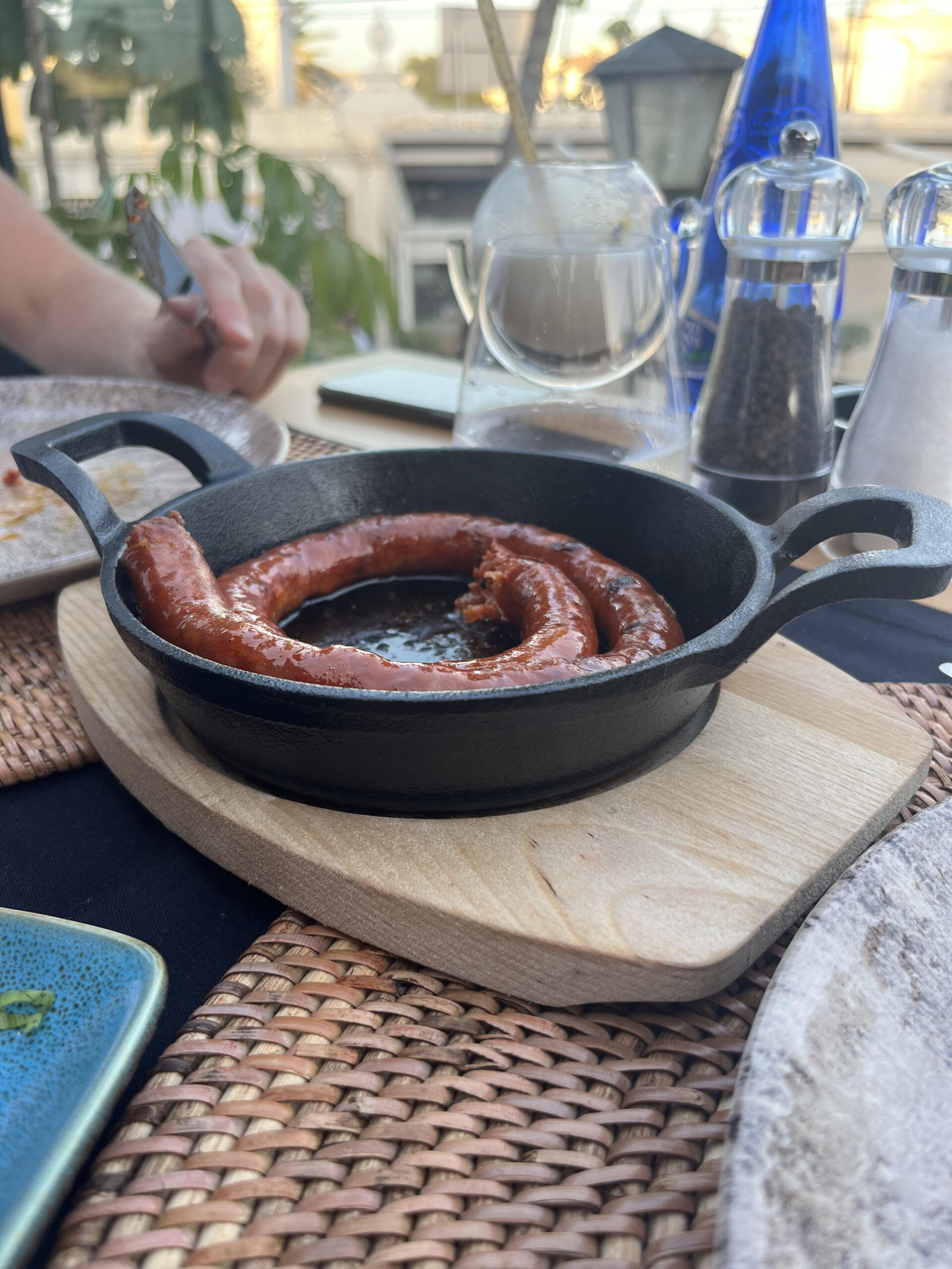 Vista de un chorizo asado al estilo español presentado en una sartén negra sobre una tabla de madera