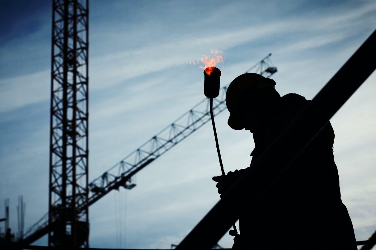 Picture of silhouette of a workman holding a torch flame with crane in background
