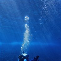 Deep sea diver in a strong blue ocean with air bubbles going upwards