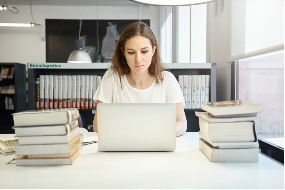 Young woman sat a laptop with books either side of her