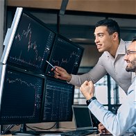 2 men sat in front of computer screens looking at trading sites