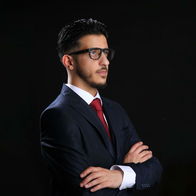 Picture of Shaffy Yaqubi with his arms crossed dressed in a dark suit with red tie and wearing glasses