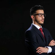 Picture of Shaffy Yaqubi with his arms crossed dressed in a dark suit with red tie and wearing glasses