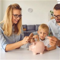 Young family sat at a table with a pink piggy bank with the child putting coins in