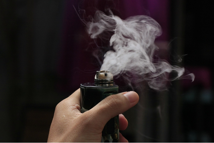 A hand holding a vape machine with smoke coming from the machine
