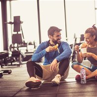 Young couple in a gym sat on the floor eating healthy food