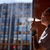 Young woman lean on a wall smoking a vape