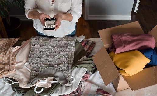 woman taking a photo on her mobile phone of items of second hand clothing