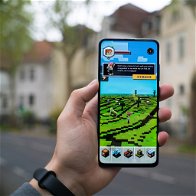 faded background picture of a town in the from a person's hand holding a mobile phone with online game on screen