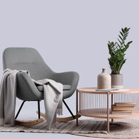 Modern grey cloth rocking chair with a grey throw over the arm in front of a wooden coffee table with a plant on