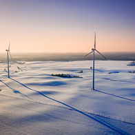 Wind turbines standing tall in a snowy Polish landscape at sunset, symbolising Poland's renewable energy progress.