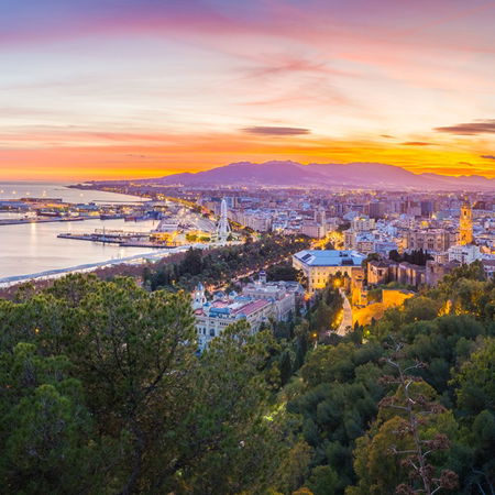 Sunset view over Málaga city and port, with the Mediterranean coastline and historic skyline illuminated at dusk