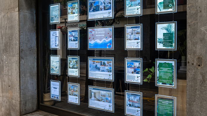 Property listings displayed in the window of a real estate agency in Spain, advertising homes for sale and rent.
