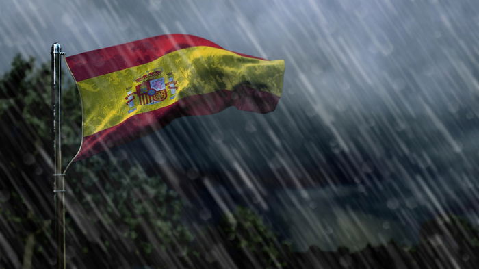 Spanish flag blowing in heavy rain and strong winds during stormy weather conditions.